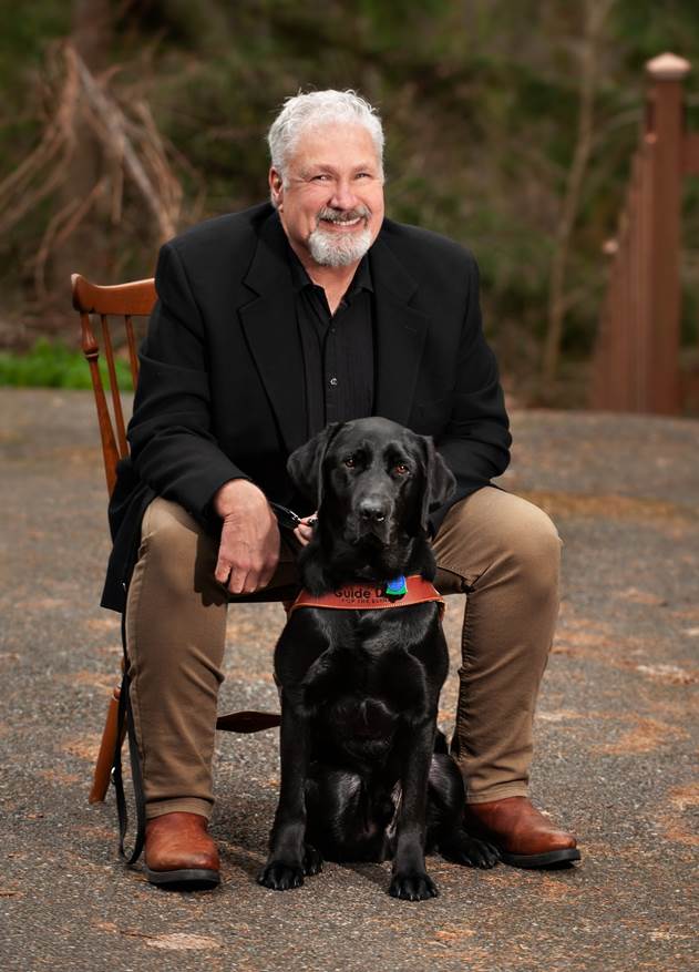 Clark Roberts seated with his guide dog, Bruno